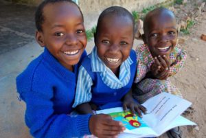 Three children from Chambuko primary school smiling wearing school uniform