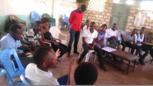 A group of youth seated i a semicircle listening to a speaker, 